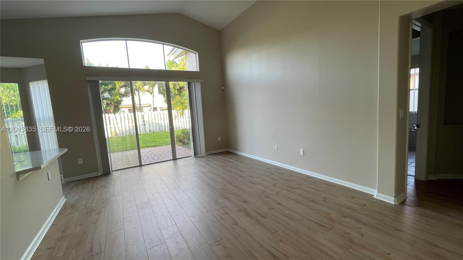 An empty living room features wood-look flooring, vaulted ceilings, and sliding glass doors to a patio — 18811 SW 29th Ct, Miramar FL 33029, MIRAMAR, FL