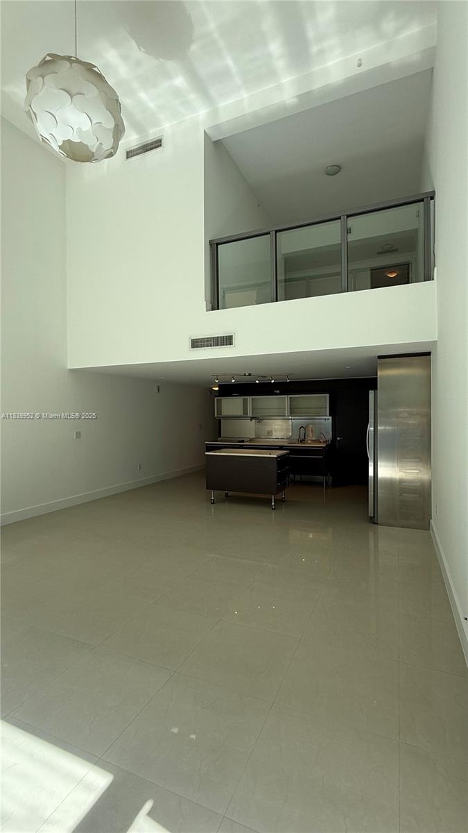 A modern, high-ceilinged living area features a kitchen with a rolling island and a lofted balcony — 6000 Collins Ave # 323, Miami Beach FL 33140, MIAMI BEACH, FL