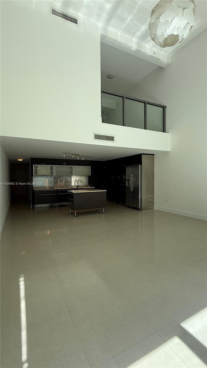 A modern kitchen with dark cabinetry and a rolling island sits beneath a high ceiling — 6000 Collins Ave # 323, Miami Beach FL 33140, MIAMI BEACH, FL