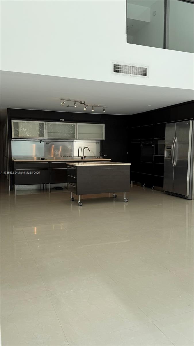 A modern kitchen features dark cabinetry, a rolling island, stainless steel appliances, and tile flooring — 6000 Collins Ave # 323, Miami Beach FL 33140, MIAMI BEACH, FL