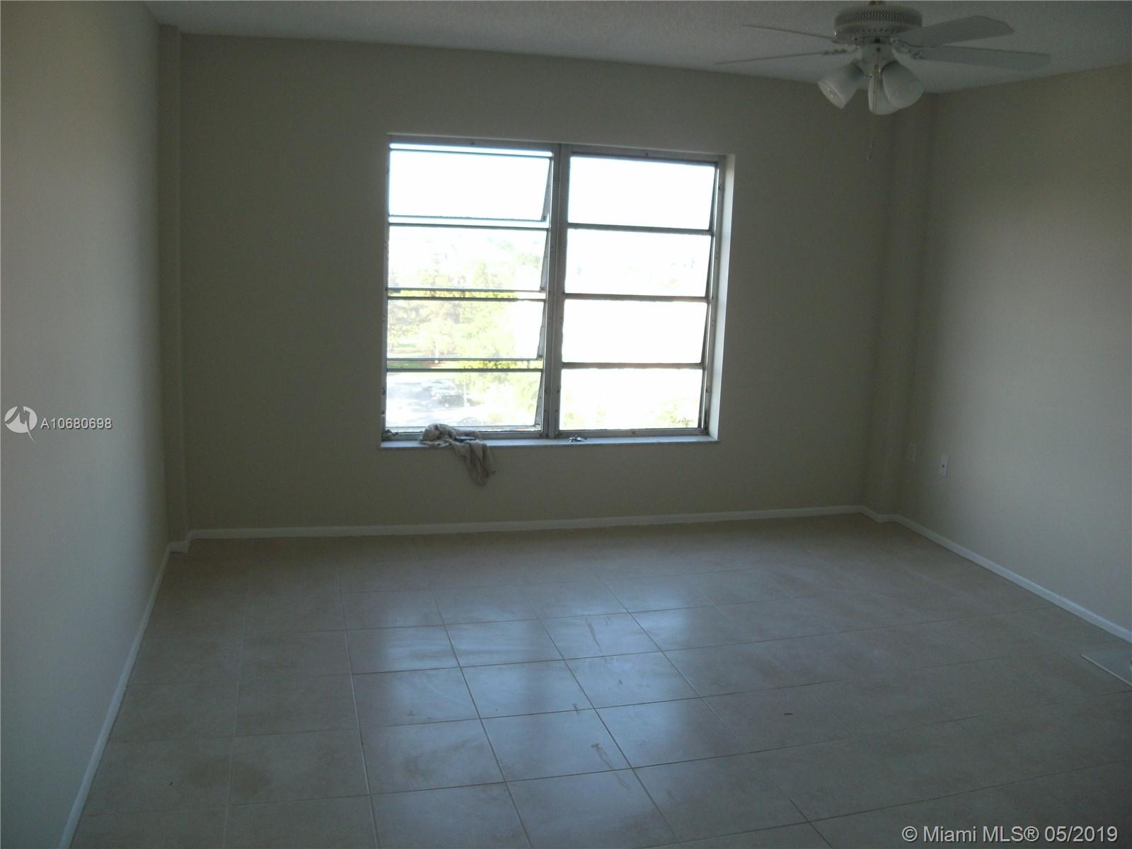 An empty room features light-colored tile flooring, beige walls, a ceiling fan, and a large window — 4174 Inverrary Dr # 911, Lauderhill FL 33319, LAUDERHILL, FL