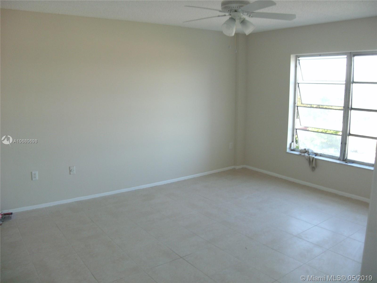 An empty room features beige walls, light-colored tile flooring, a ceiling fan, and a window — 4174 Inverrary Dr # 911, Lauderhill FL 33319, LAUDERHILL, FL