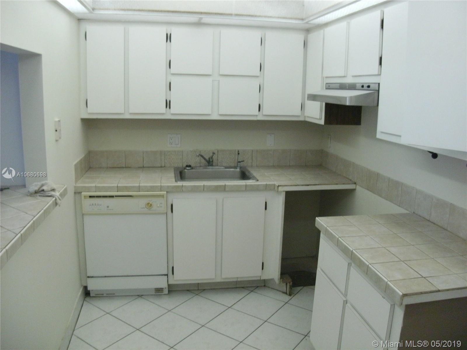 A kitchen features white cabinets, tiled countertops, a stainless steel sink, and a white dishwasher — 4174 Inverrary Dr # 911, Lauderhill FL 33319, LAUDERHILL, FL