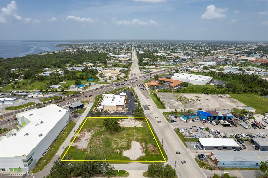An aerial view shows a vacant, rectangular lot outlined in yellow near a busy intersection — 23041 HARBORVIEW ROAD, PORT CHARLOTTE, FL