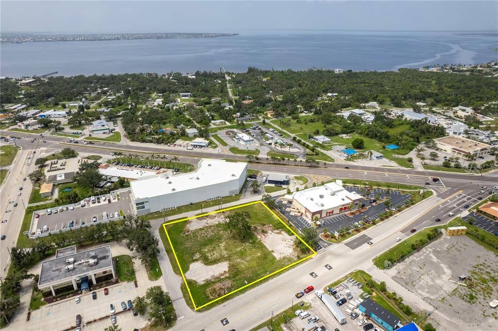 An aerial view shows a vacant rectangular lot outlined in yellow near a coastal road — 23041 HARBORVIEW ROAD, PORT CHARLOTTE, FL
