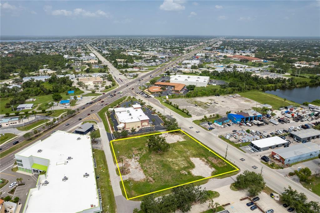 An aerial view shows a vacant, rectangular grass lot outlined in yellow near a road — 23041 HARBORVIEW ROAD, PORT CHARLOTTE, FL