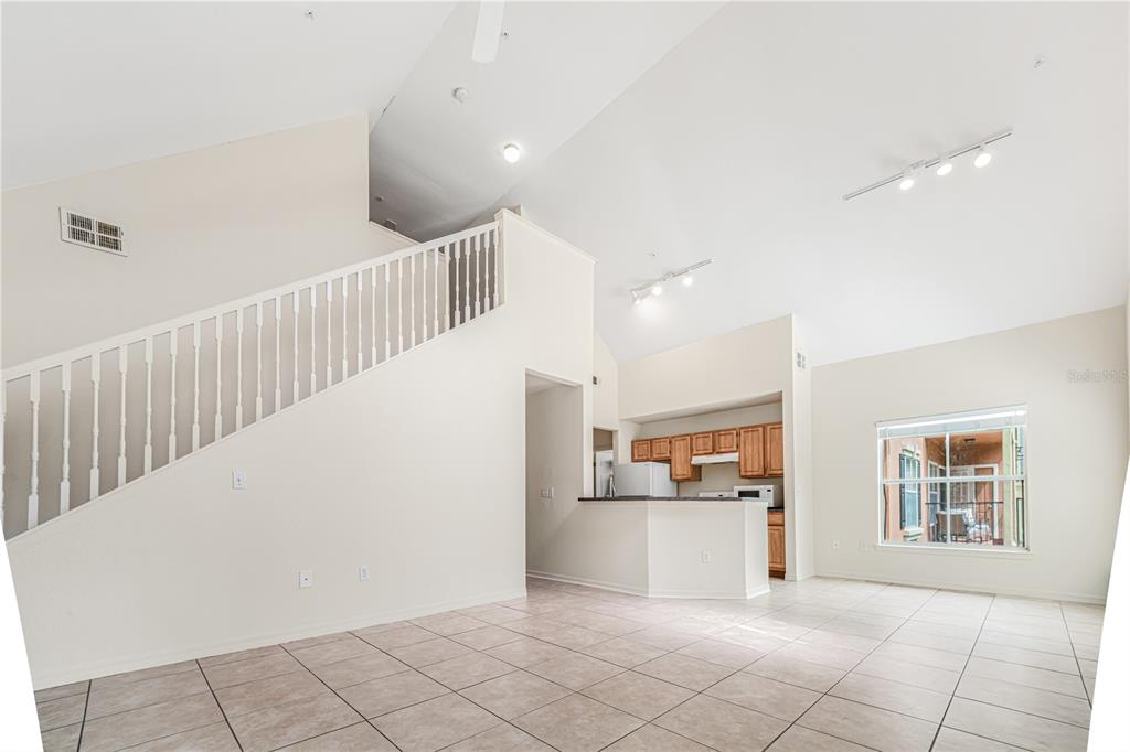 An open-concept living area with tiled floors, a staircase, and a kitchen with wooden cabinets — 6025 WESTGATE DRIVE UNIT 2527, ORLANDO, FL