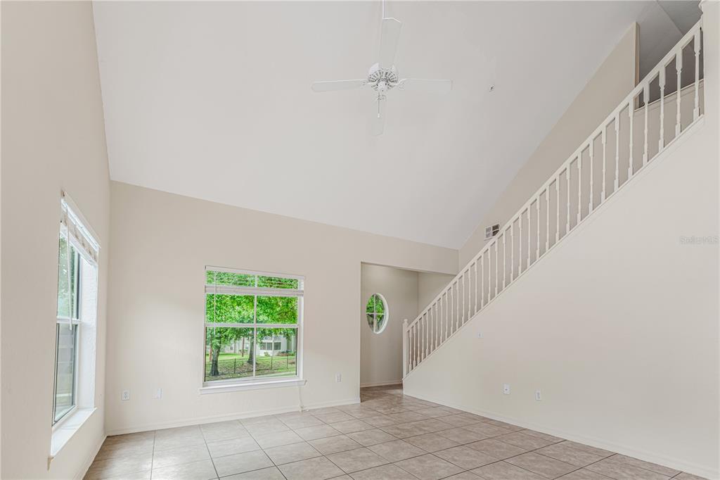 An empty room with vaulted ceilings, tile flooring, and a staircase with a white railing — 6025 WESTGATE DRIVE UNIT 2527, ORLANDO, FL