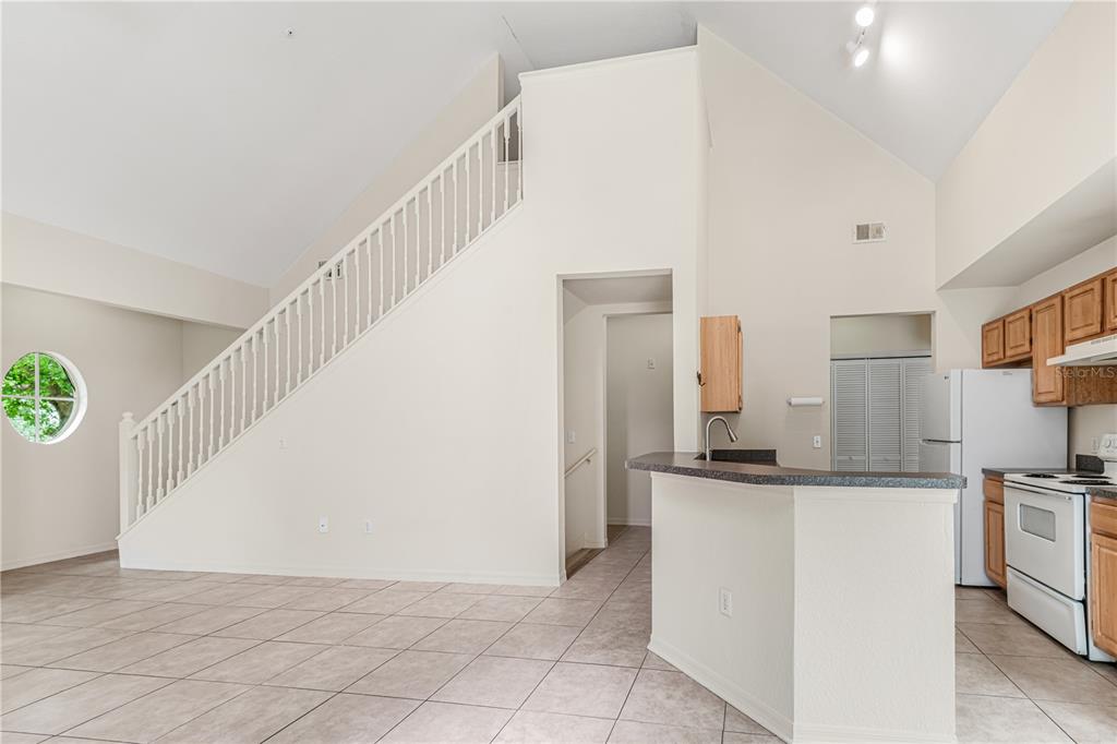A kitchen with white appliances and a breakfast bar opens to a living area with stairs — 6025 WESTGATE DRIVE UNIT 2527, ORLANDO, FL