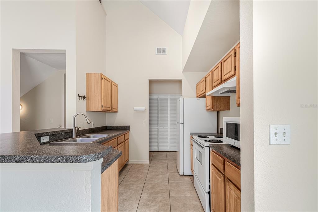 A kitchen with light wood cabinets, dark countertops, white appliances, and tiled flooring — 6025 WESTGATE DRIVE UNIT 2527, ORLANDO, FL