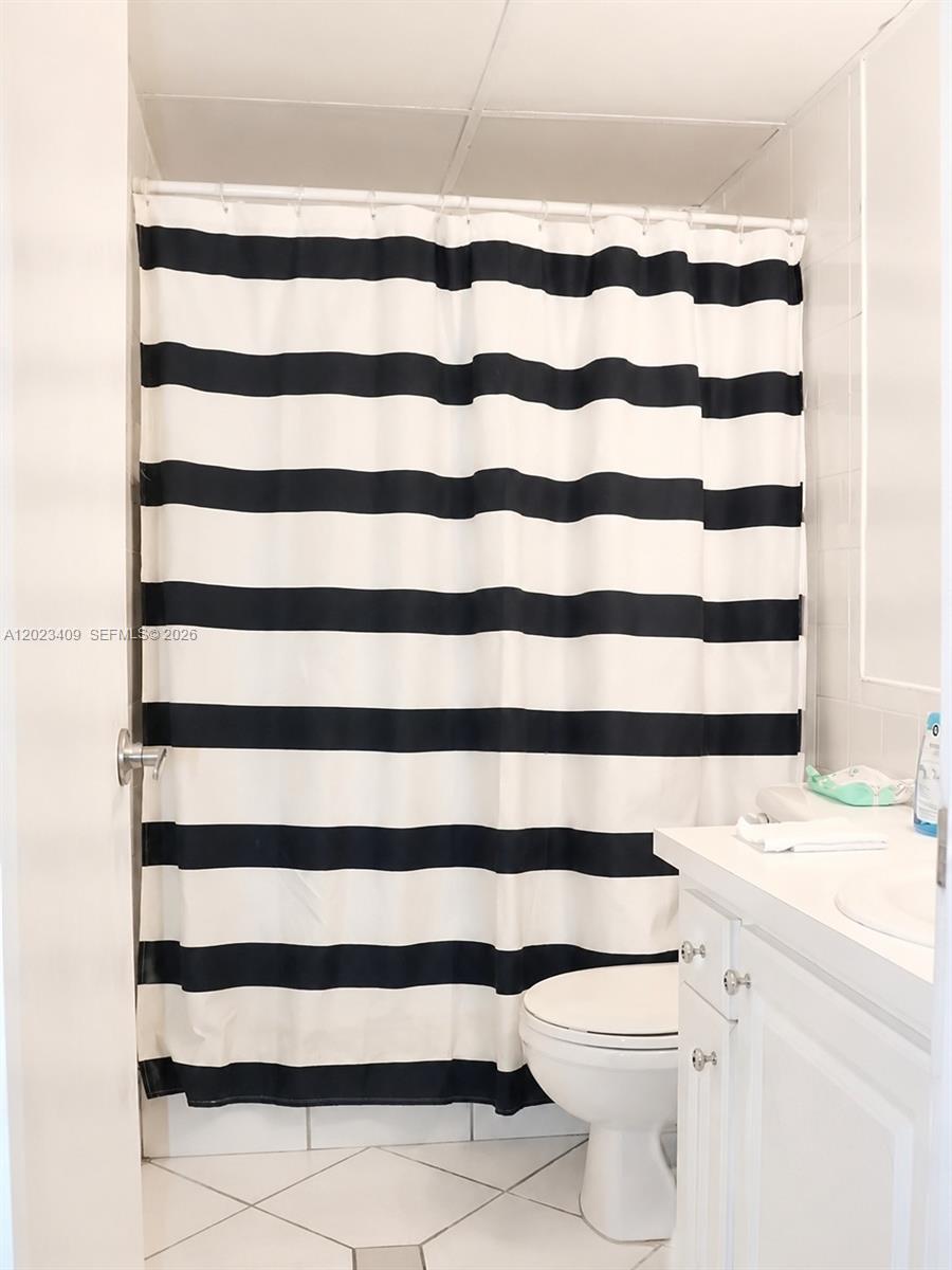 A bathroom features a black and white striped shower curtain, a white vanity, and tiled flooring — 500 NE 2nd St # 115, Dania Beach FL 33004, DANIA BEACH, FL