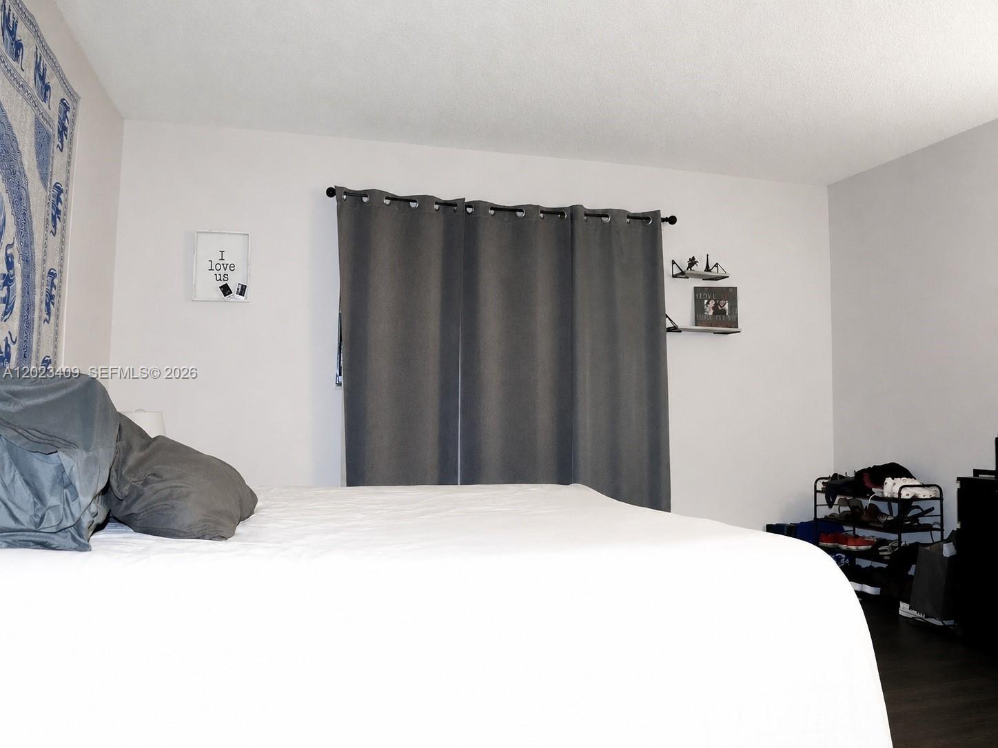 A bedroom features a bed with grey pillows, dark curtains, and a shoe rack — 500 NE 2nd St # 115, Dania Beach FL 33004, DANIA BEACH, FL