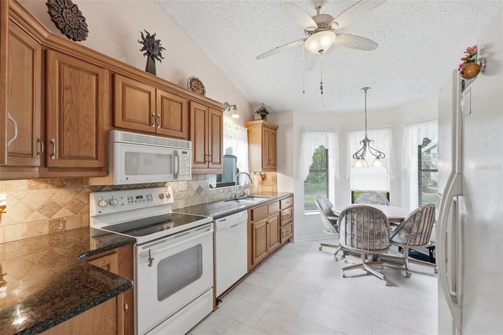 A kitchen with oak cabinets, granite countertops, white appliances, and an adjacent dining nook — 3254 LORI LANE, NEW PORT RICHEY, FL