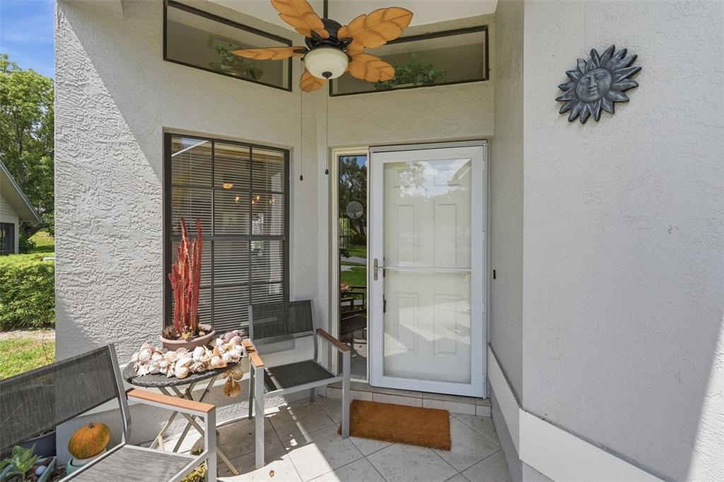 A covered entryway features a white storm door, a ceiling fan, and patio furniture — 3254 LORI LANE, NEW PORT RICHEY, FL