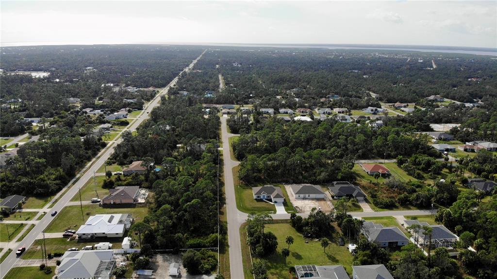 An aerial view shows a suburban neighborhood with houses surrounded by dense trees and roads — 17497 BILLIAR AVENUE, PORT CHARLOTTE, FL