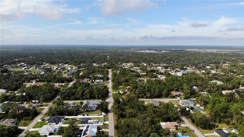 An aerial view shows a residential neighborhood with houses surrounded by dense trees and vegetation — 17497 BILLIAR AVENUE, PORT CHARLOTTE, FL