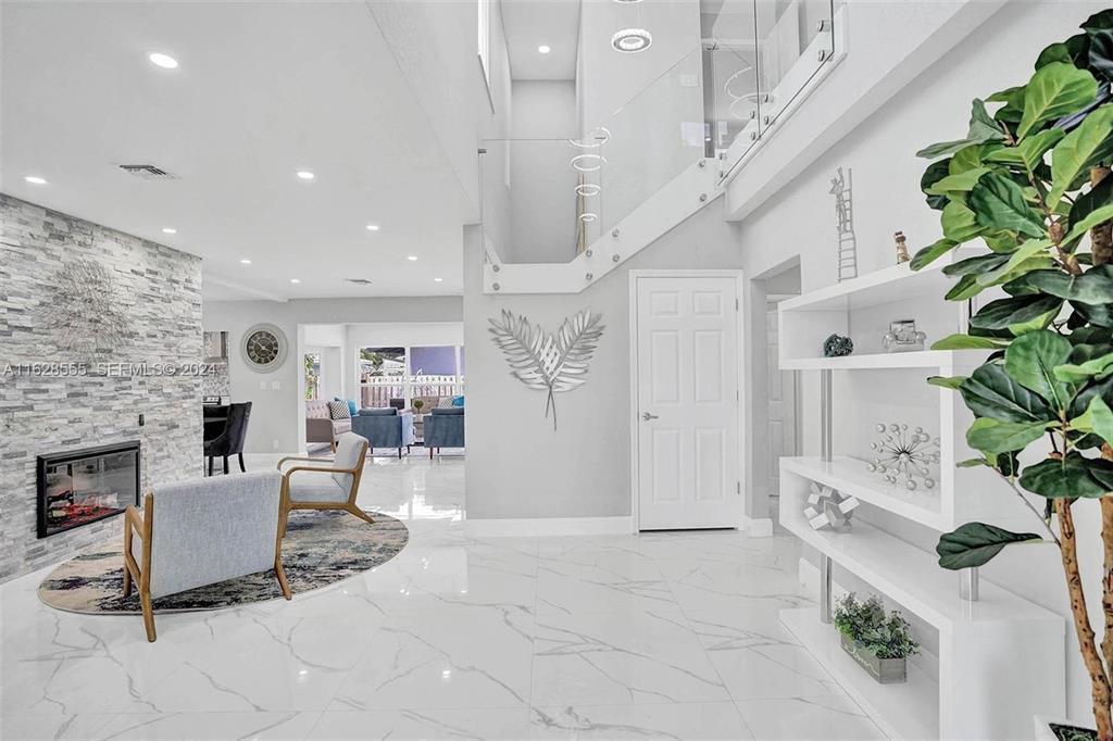 A bright, modern living room features white marble floors, a stone fireplace, and a glass staircase — 3421 Dover Road, Pompano Beach FL 33062, POMPANO BEACH, FL