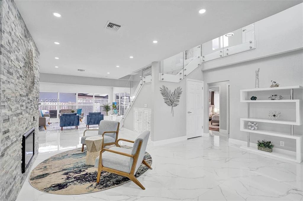 A modern living room features marble floors, a stone fireplace, and a glass-railed staircase — 3421 Dover Road, Pompano Beach FL 33062, POMPANO BEACH, FL