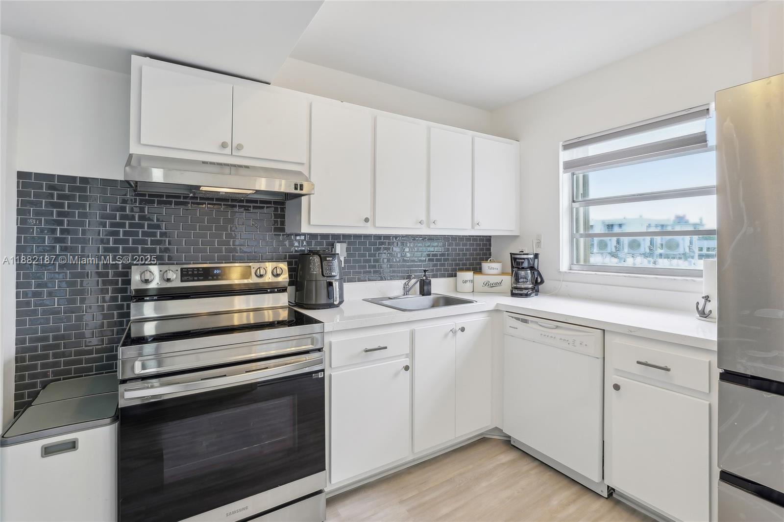 A kitchen features white cabinets, stainless steel appliances, and a dark gray subway tile backsplash — 1345 West Avenue # 304, Miami Beach FL 33139, MIAMI BEACH, FL