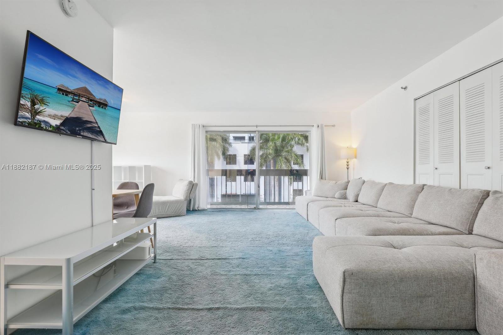 A living room features a large sectional sofa, blue carpeting, and a sliding glass door — 1345 West Avenue # 304, Miami Beach FL 33139, MIAMI BEACH, FL