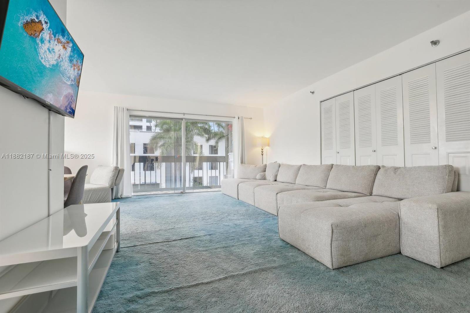 A living room features a large sectional sofa, blue carpeting, and a sliding glass door — 1345 West Avenue # 304, Miami Beach FL 33139, MIAMI BEACH, FL