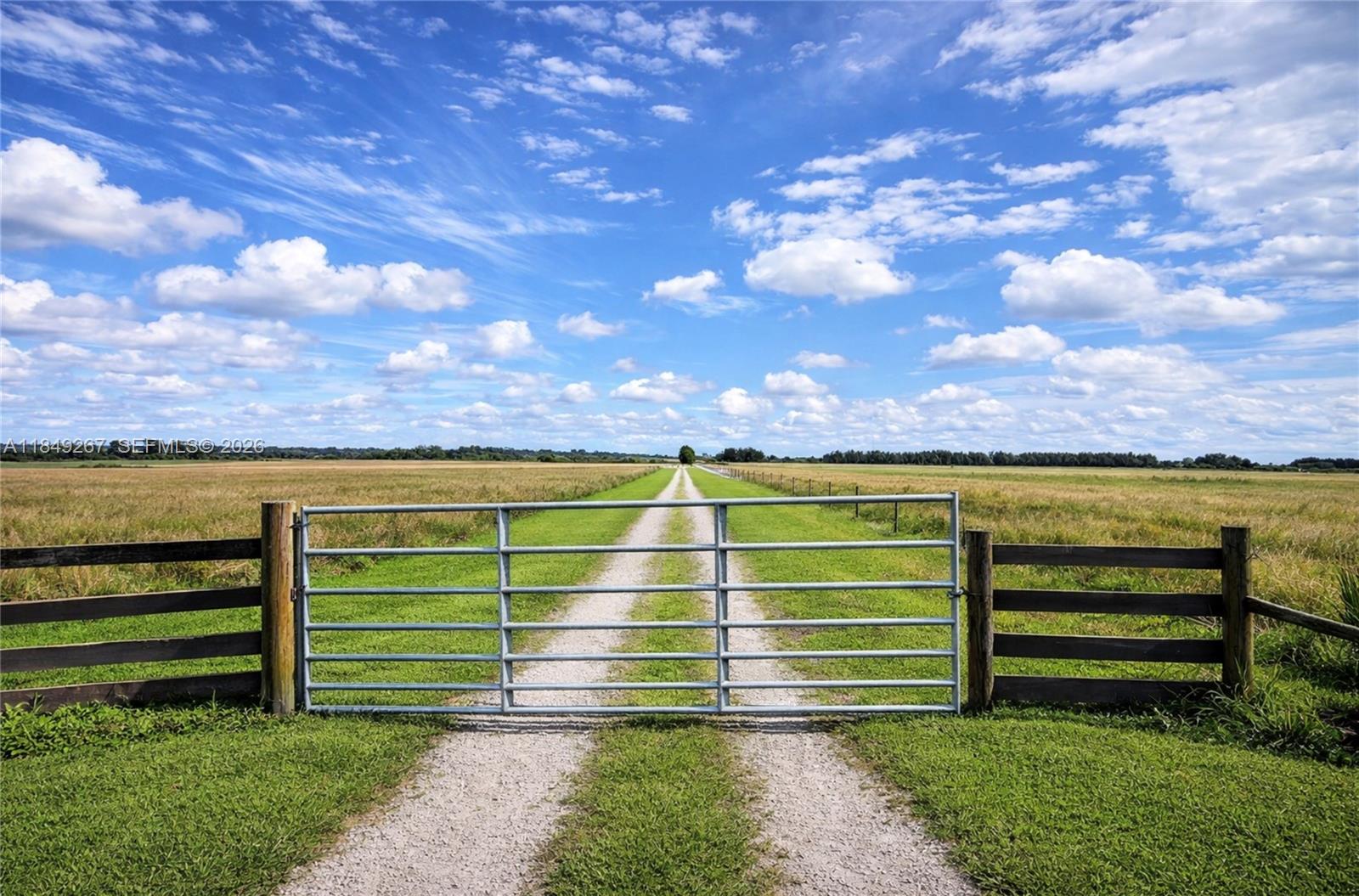 A metal gate opens onto a long gravel driveway leading through a large, grassy field — 595 N HEADER CANAL ROAD, Fort Pierce FL 34945, FORT PIERCE, FL