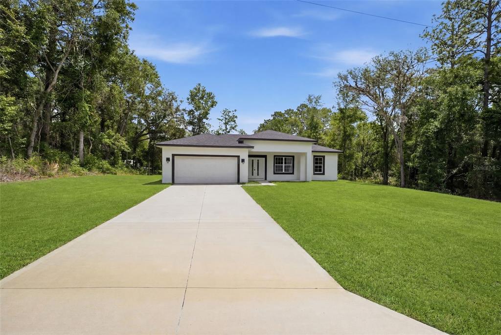 A single-story house with a white exterior, dark roof, and concrete driveway sits on grass — 8511 N GOLFVIEW DRIVE, CITRUS SPRINGS, FL