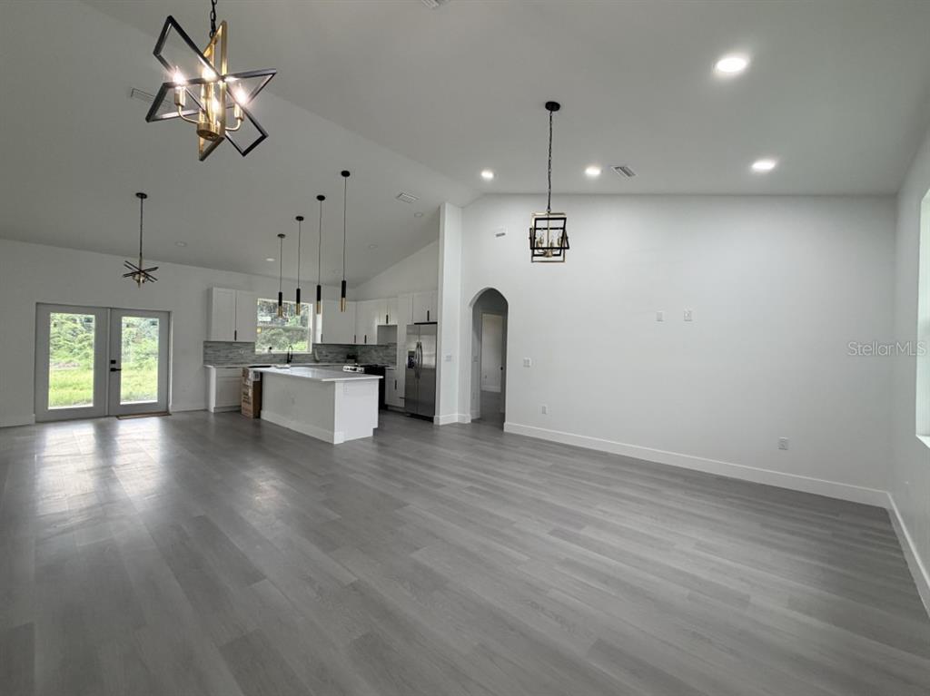 An open-concept living area features a kitchen with white cabinets, a central island, and wood-look flooring — 3500 SE 484, BELLEVIEW, FL