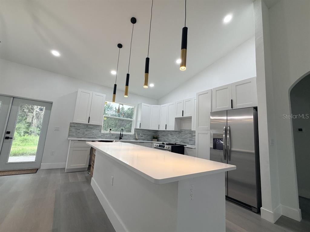 A modern kitchen features white cabinetry, a large quartz island, and four pendant lights — 3500 SE 484, BELLEVIEW, FL