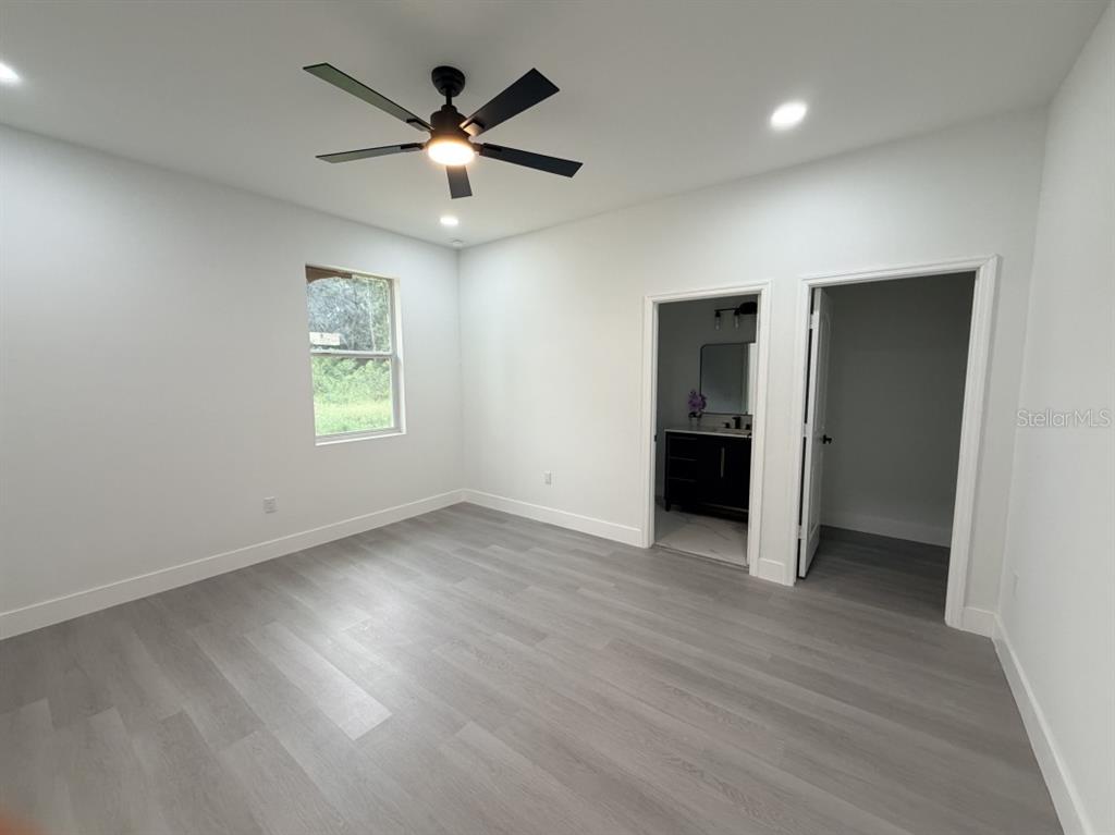 A bedroom with light gray wood-look flooring, white walls, a ceiling fan, and two doorways — 3500 SE 484, BELLEVIEW, FL