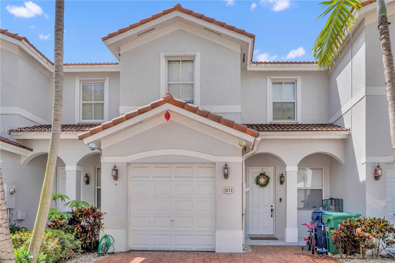The exterior of a two-story townhouse features a garage, a front entrance, and palm trees — 1024 NE 208th St, Miami FL 33179, MIAMI, FL