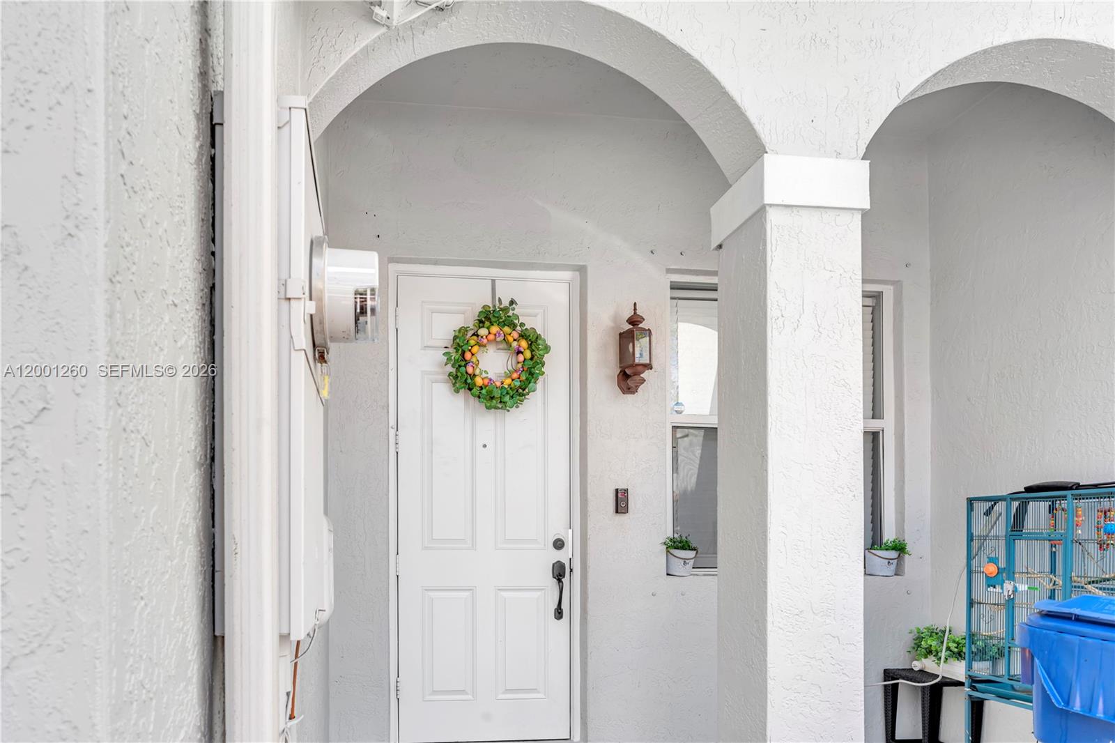 A white front door with an Easter wreath sits under an arched entryway — 1024 NE 208th St, Miami FL 33179, MIAMI, FL