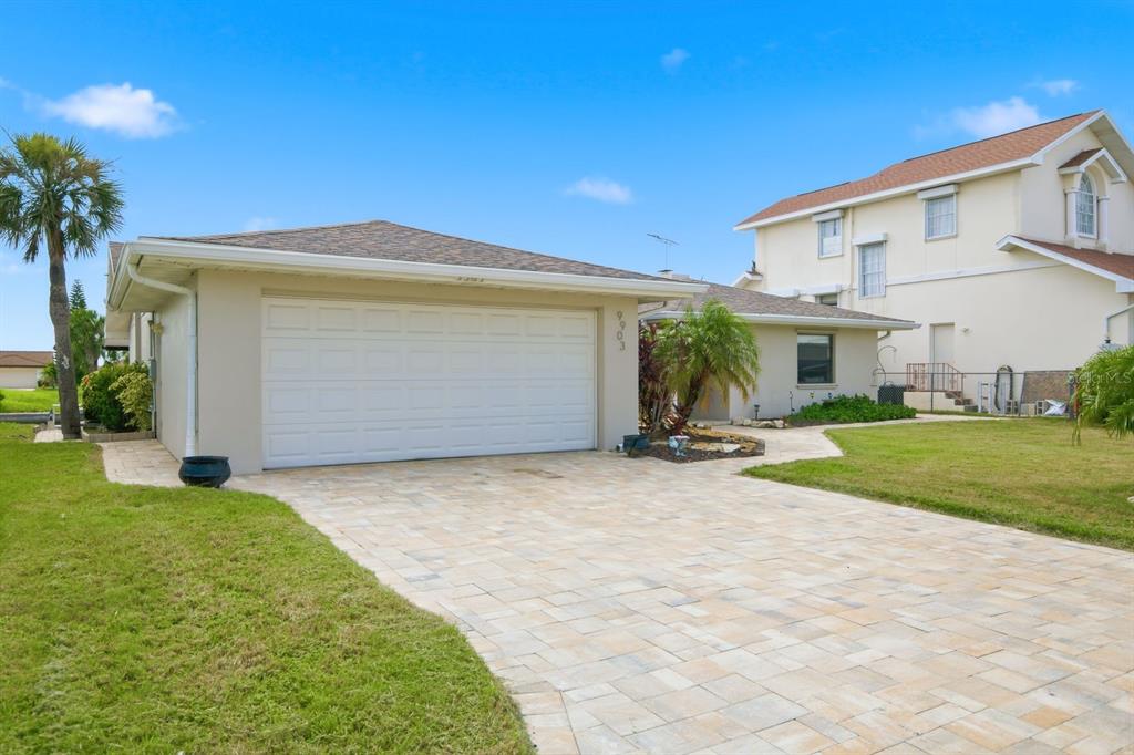 A single-story house with a paved driveway, a two-car garage, and a neighboring two-story home — 9903 SAN SEBASTIAN WAY, PORT RICHEY, FL