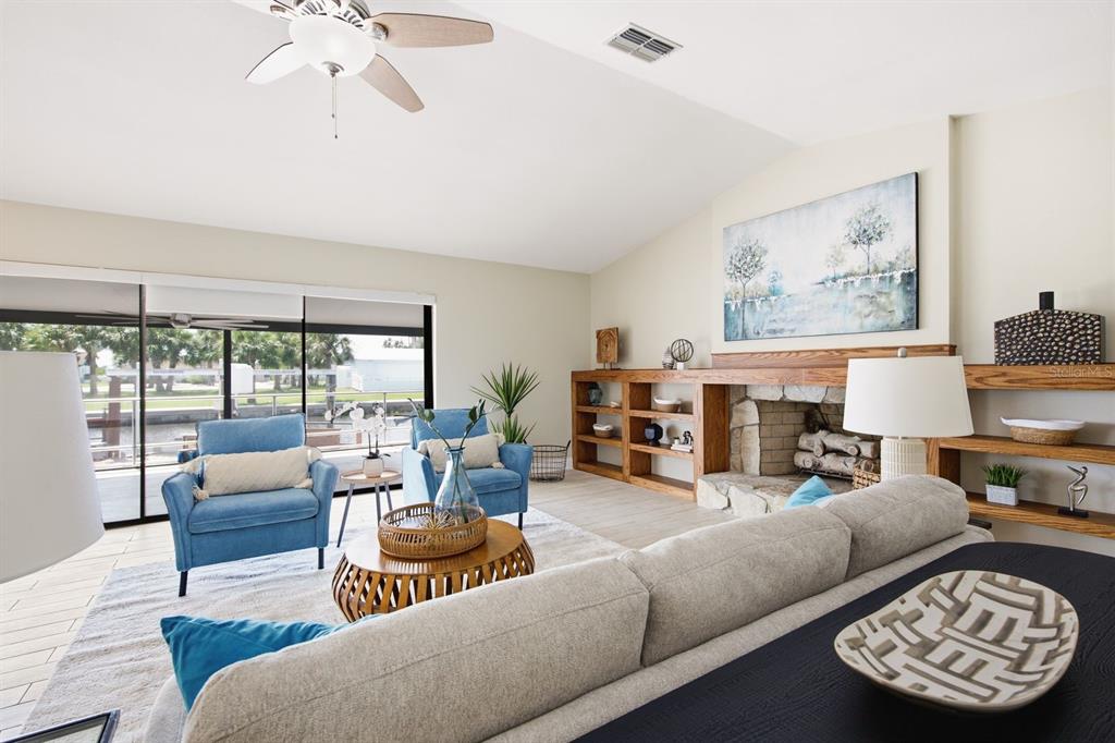A living room features a stone fireplace, built-in wooden shelving, blue armchairs, and sliding glass doors — 9903 SAN SEBASTIAN WAY, PORT RICHEY, FL