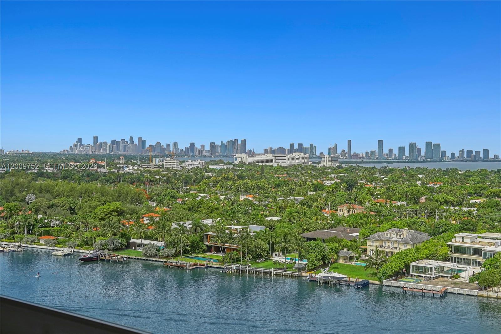 An elevated view of a waterfront neighborhood with luxury homes and a distant city skyline — 4747 Collins Ave # 1503, Miami Beach FL 33140, MIAMI BEACH, FL