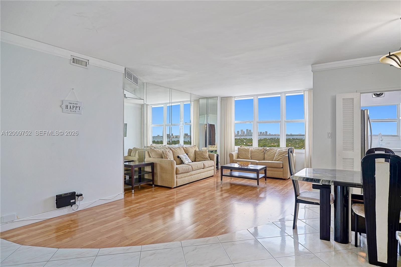 A living room features hardwood floors, mirrored walls, and large windows with a city view — 4747 Collins Ave # 1503, Miami Beach FL 33140, MIAMI BEACH, FL