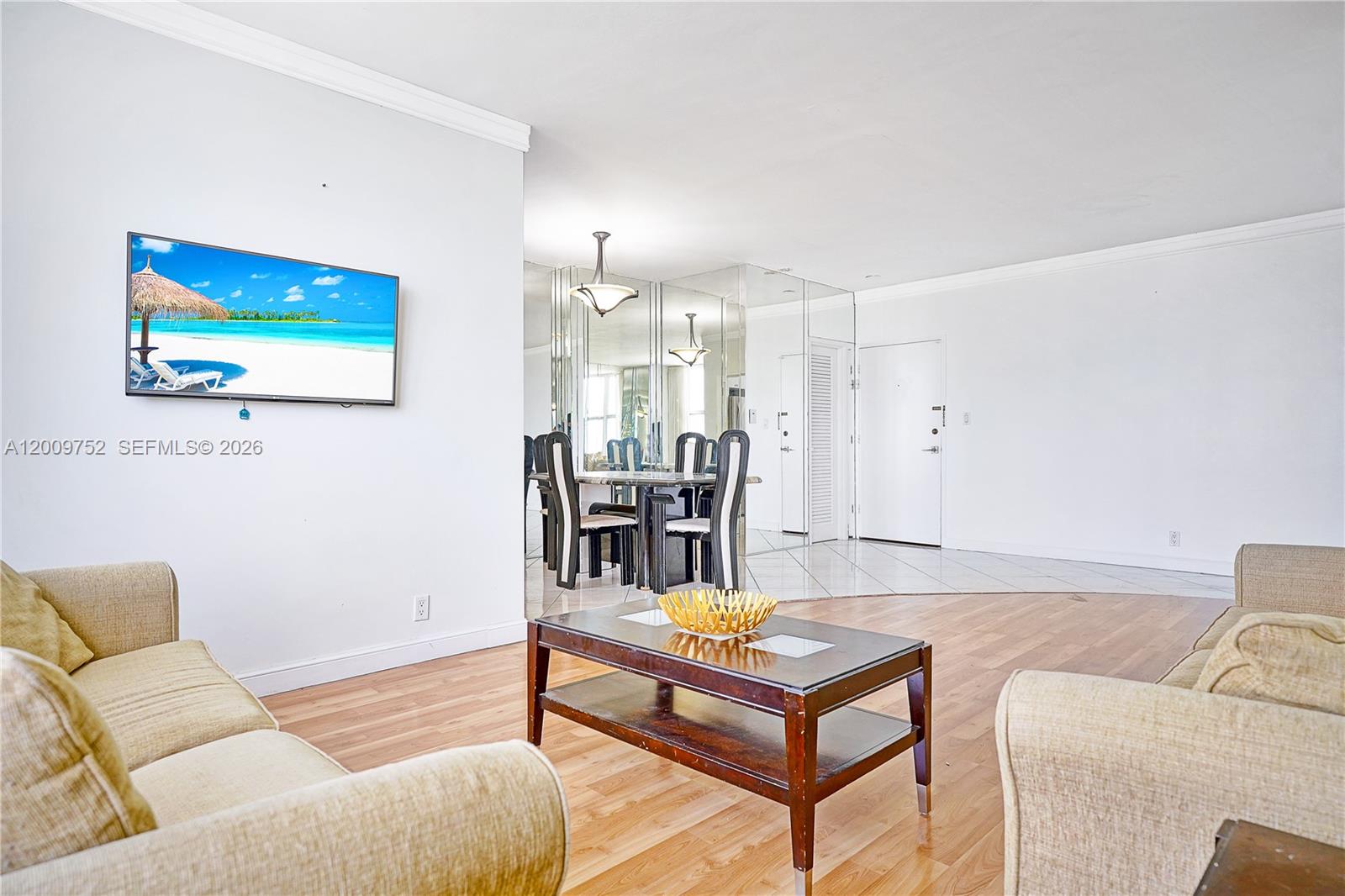A living room with light wood flooring, beige sofas, and a mirrored dining area — 4747 Collins Ave # 1503, Miami Beach FL 33140, MIAMI BEACH, FL