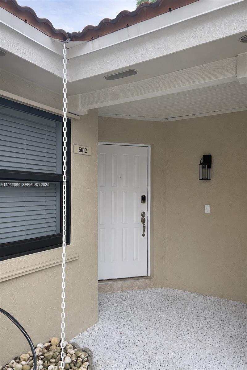 A white front door is visible next to a rain chain hanging from the roof — 6012 NW 172nd Terr Cir, Hialeah FL 33015, HIALEAH, FL