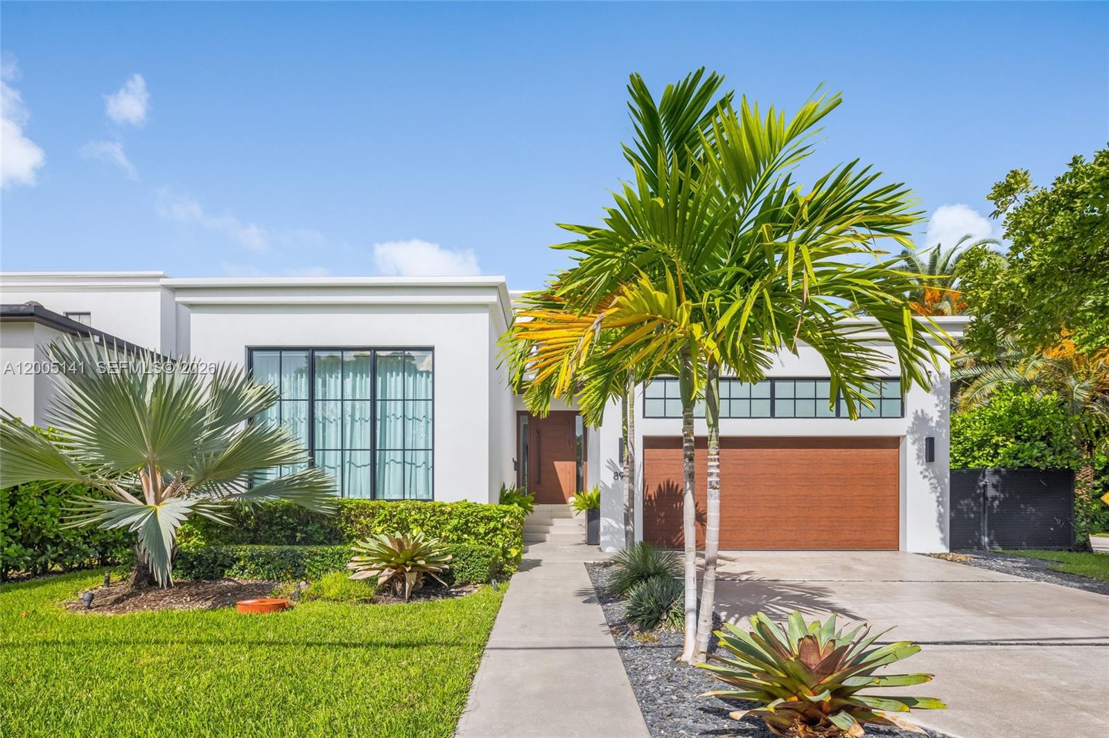 A modern white house features a wooden garage door, large windows, and palm trees — 895 NE 76th St, Miami FL 33138, MIAMI, FL