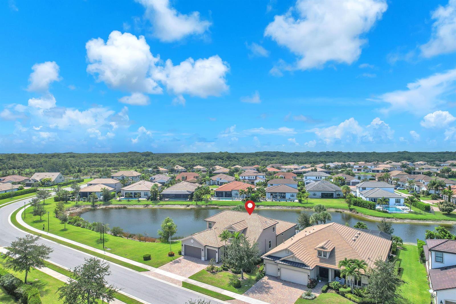 An aerial view shows a suburban neighborhood with houses surrounding a central pond — 507 Sonoma Isles Circle, Jupiter FL 33478, JUPITER, FL
