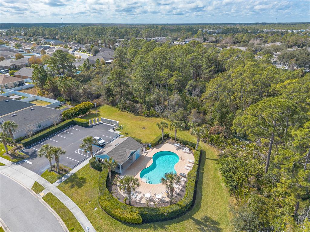 An aerial view shows a community swimming pool, clubhouse, and parking lot near a forest — 2612 STAR CORAL LANE, NEW SMYRNA BEACH, FL