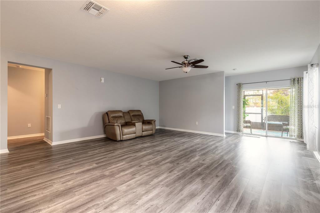 A spacious living room features light gray walls, wood-look flooring, a ceiling fan, and sliding doors — 2612 STAR CORAL LANE, NEW SMYRNA BEACH, FL