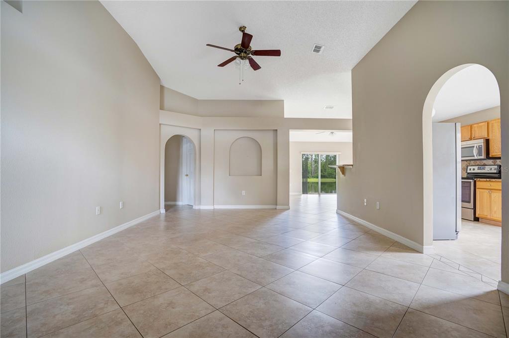 An open-concept living area features beige walls, tile flooring, a ceiling fan, and arched doorways — 1845 CORNER MEADOW CIRCLE, ORLANDO, FL