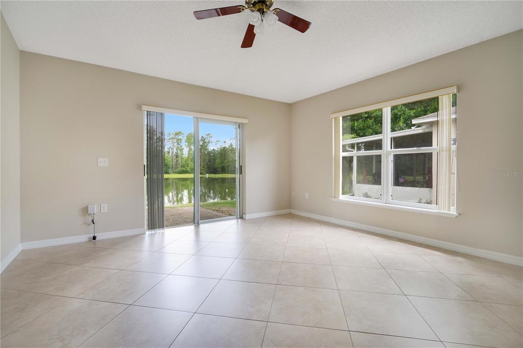 An empty living room features beige tile flooring, a ceiling fan, and sliding glass doors — 1845 CORNER MEADOW CIRCLE, ORLANDO, FL