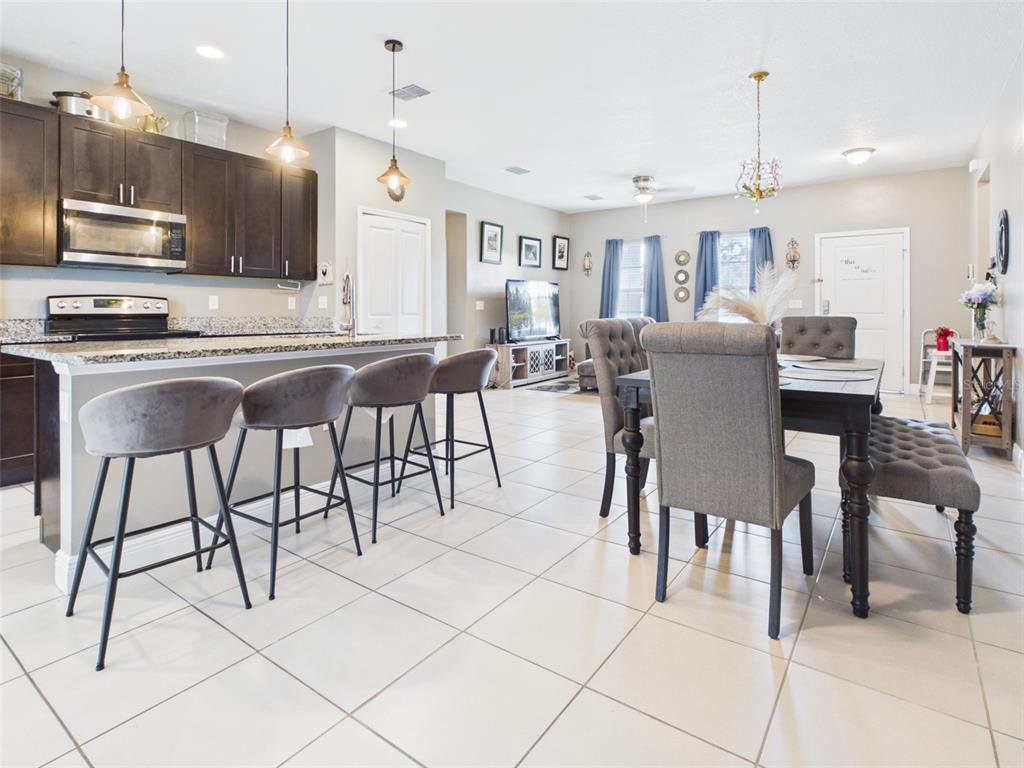 An open-concept kitchen and dining area features dark cabinetry, granite countertops, and tile flooring — 14942 SW 24TH CIRCLE, OCALA, FL