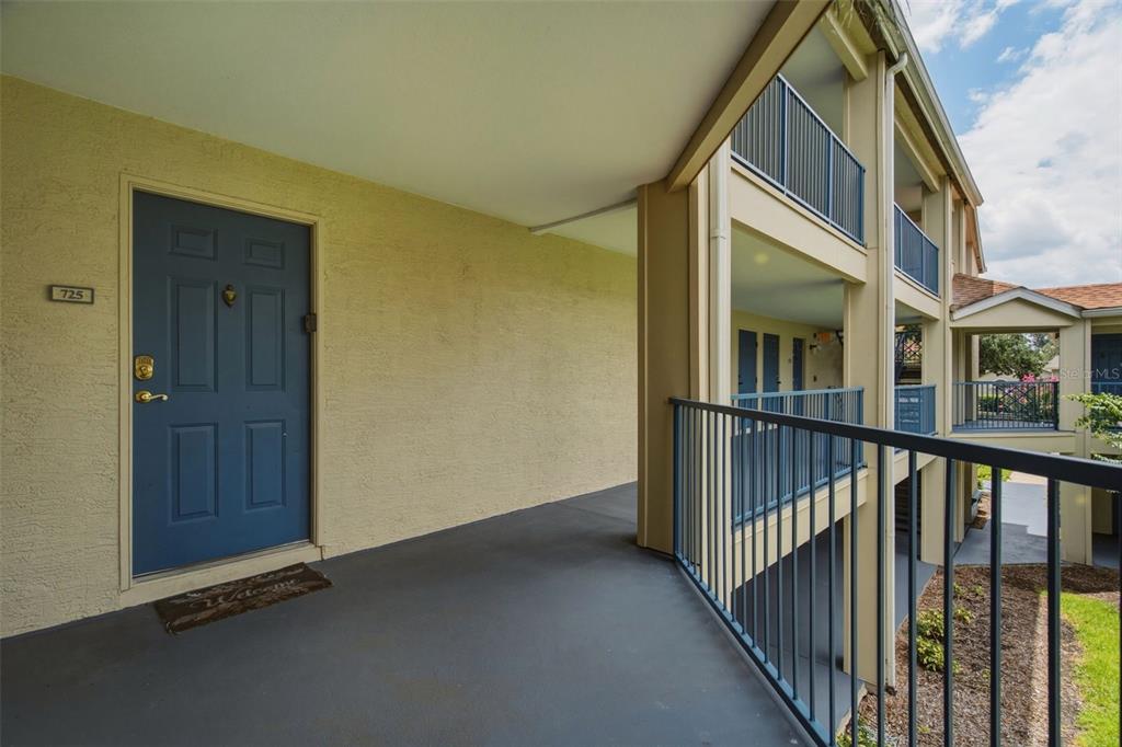 A blue front door with a welcome mat sits on a covered outdoor apartment walkway — 7300 WESTPOINTE BOULEVARD UNIT 725, ORLANDO, FL