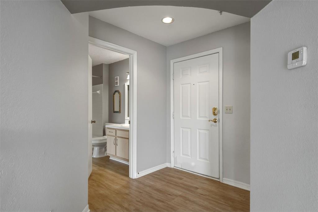 An entryway with wood-look flooring leads to a white front door and a bathroom — 7300 WESTPOINTE BOULEVARD UNIT 725, ORLANDO, FL