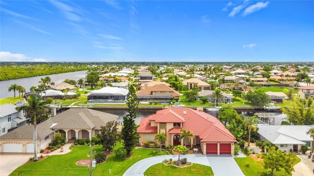 An aerial view shows suburban houses with red-tiled roofs situated along a canal — 134 SEVILLE PLACE SW, PORT CHARLOTTE, FL