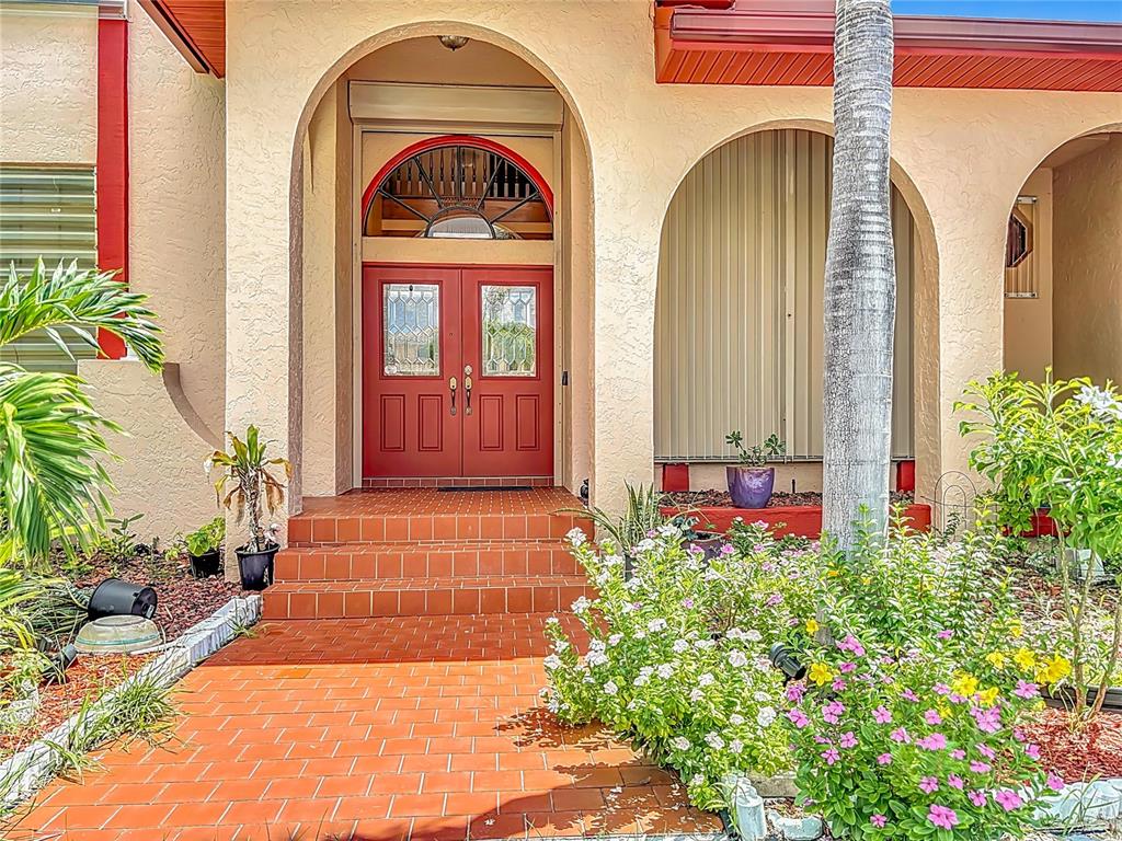 A red double front door with a decorative arched transom sits atop brick steps — 134 SEVILLE PLACE SW, PORT CHARLOTTE, FL