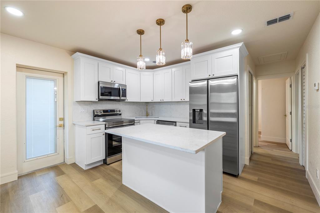 A kitchen features white cabinetry, stainless steel appliances, a center island, and light wood flooring — 5538 6TH AVENUE N, ST PETERSBURG, FL